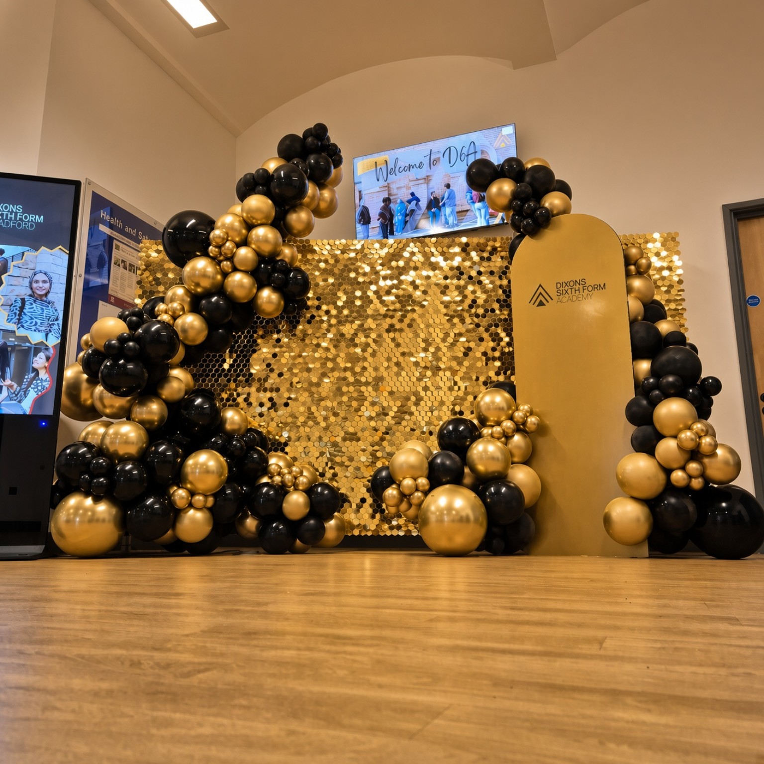 Gold shimmer wall and branded board with black and gold balloons