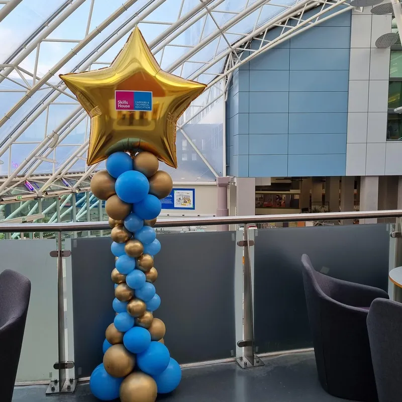 Blue and gold balloon tower topped with a gold star balloon at an indoor venue