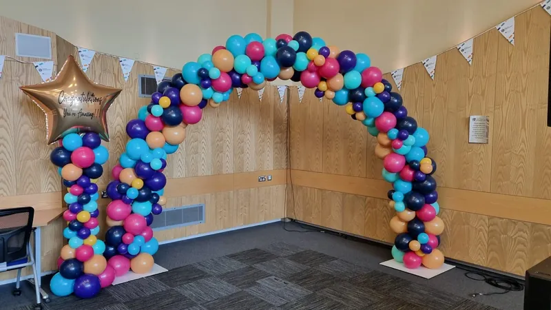 Indoor fancy balloon arch in pink, teal, orange and purple with one matching tower topped by a gold star