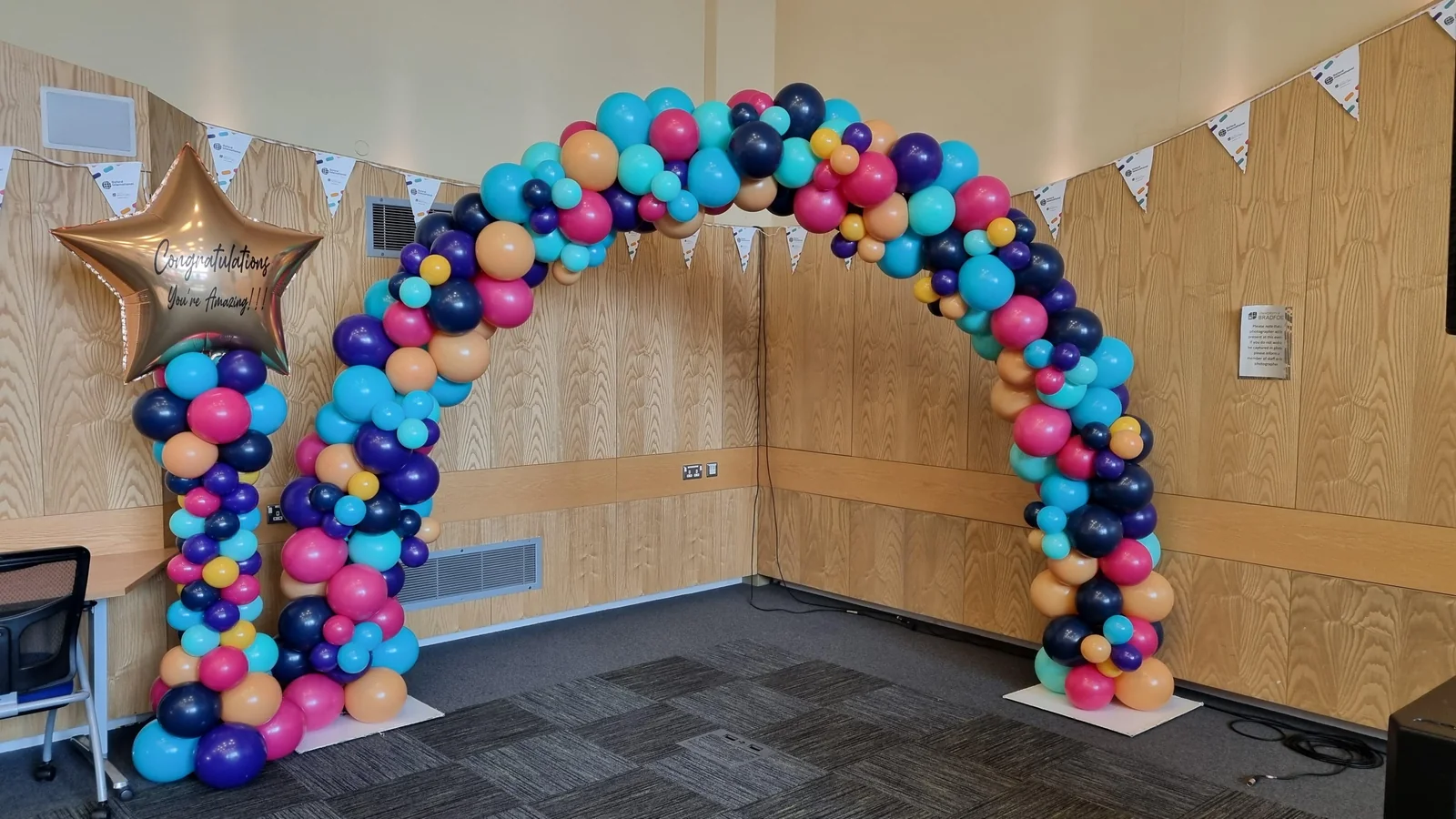 Indoor fancy balloon arch in pink, teal, orange and purple with one matching tower topped by a gold star